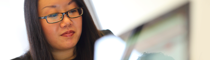 A person wearing glasses is looking at a computer screen with a focused expression. They appear to be working or studying in an office environment.