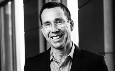 Black and white headshot of a smiling person wearing glasses and a business suit.