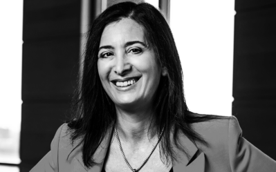 BW FacultyPhotos Nancy Rothbard Headshot of a smiling person with long hair wearing a blazer and necklace, in a professional setting with blurred background.